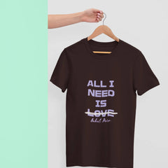 Brown t-shirt with 'All I Need is Love' text on a hanger against a light background