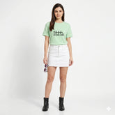 Woman wearing a light green t-shirt with text and a white skirt on a white background