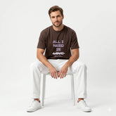 Man wearing a brown t-shirt with 'All I Need is Love' text, sitting on a white chair against a light gray background.