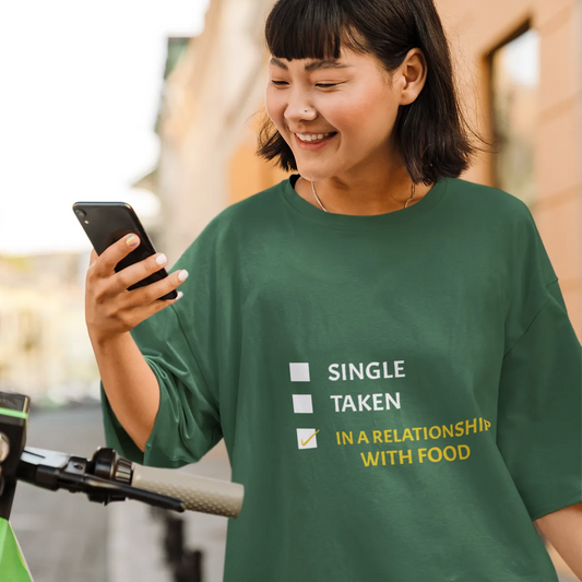 Person wearing a green t-shirt with humorous relationship status text, using a smartphone outdoors.