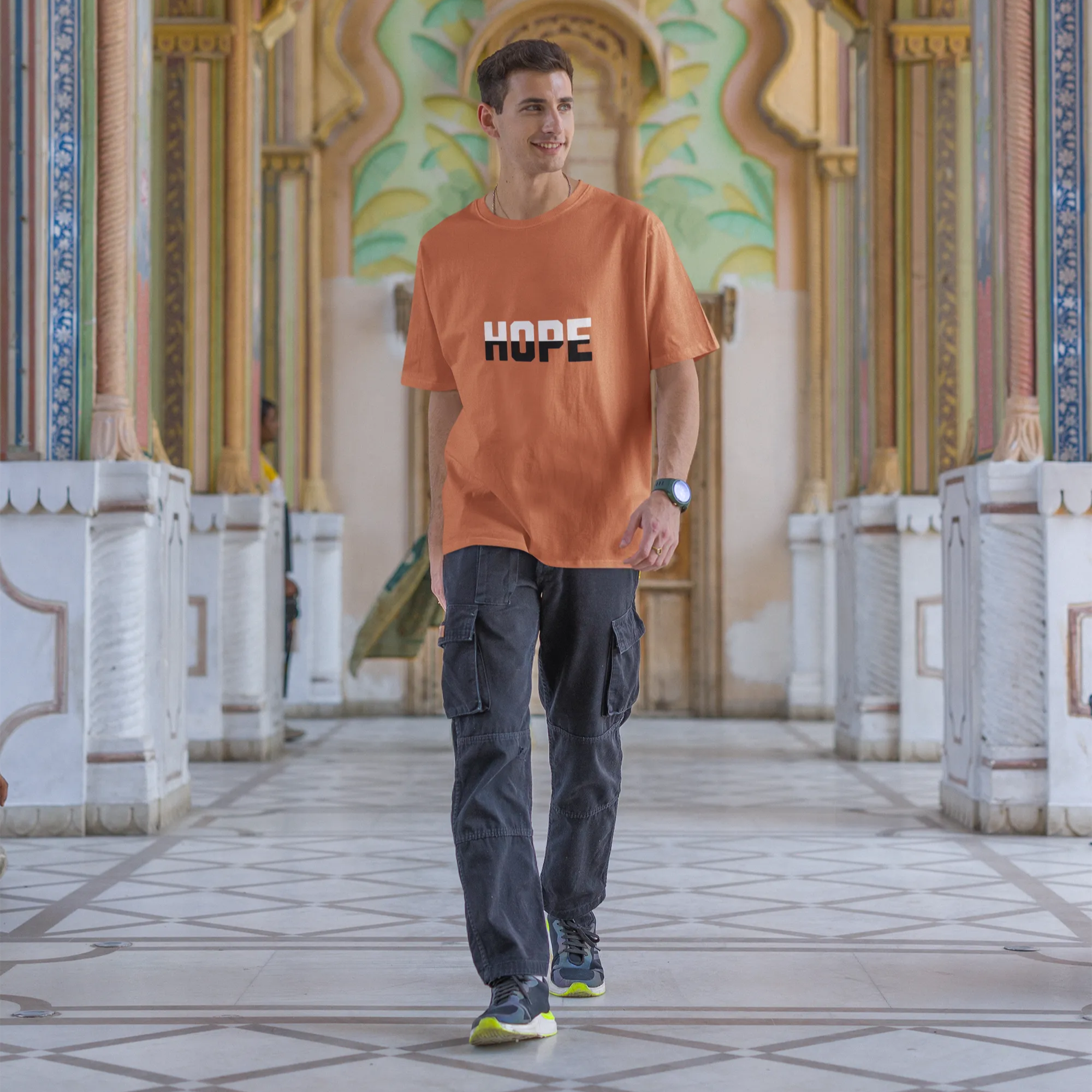 Man wearing an orange t-shirt with 'HOPE' printed on it, standing in a decorative architectural setting.