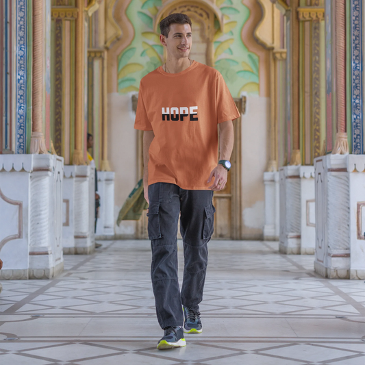 Man wearing an orange t-shirt with 'HOPE' printed on it, standing in a decorative architectural setting.