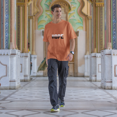 Man wearing an orange t-shirt with 'HOPE' printed on it, standing in a decorative architectural setting.
