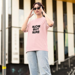 Person wearing a pink t-shirt with text, light blue jeans, and white sneakers in an urban setting.