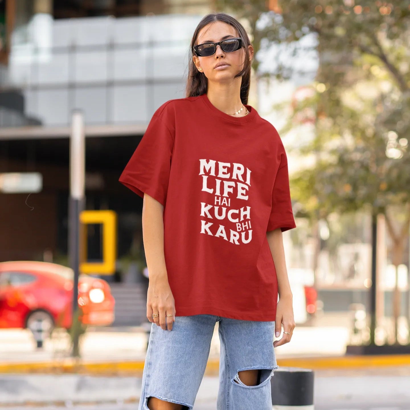 Person wearing a red oversized t-shirt with text and ripped jeans on a street.