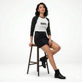 Woman sitting on a stool wearing a black and white 'BORED.' shirt, black skirt, and black boots on a white background.