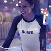 Woman wearing a shirt with 'BORED.' text in a colorful, possibly amusement park setting.