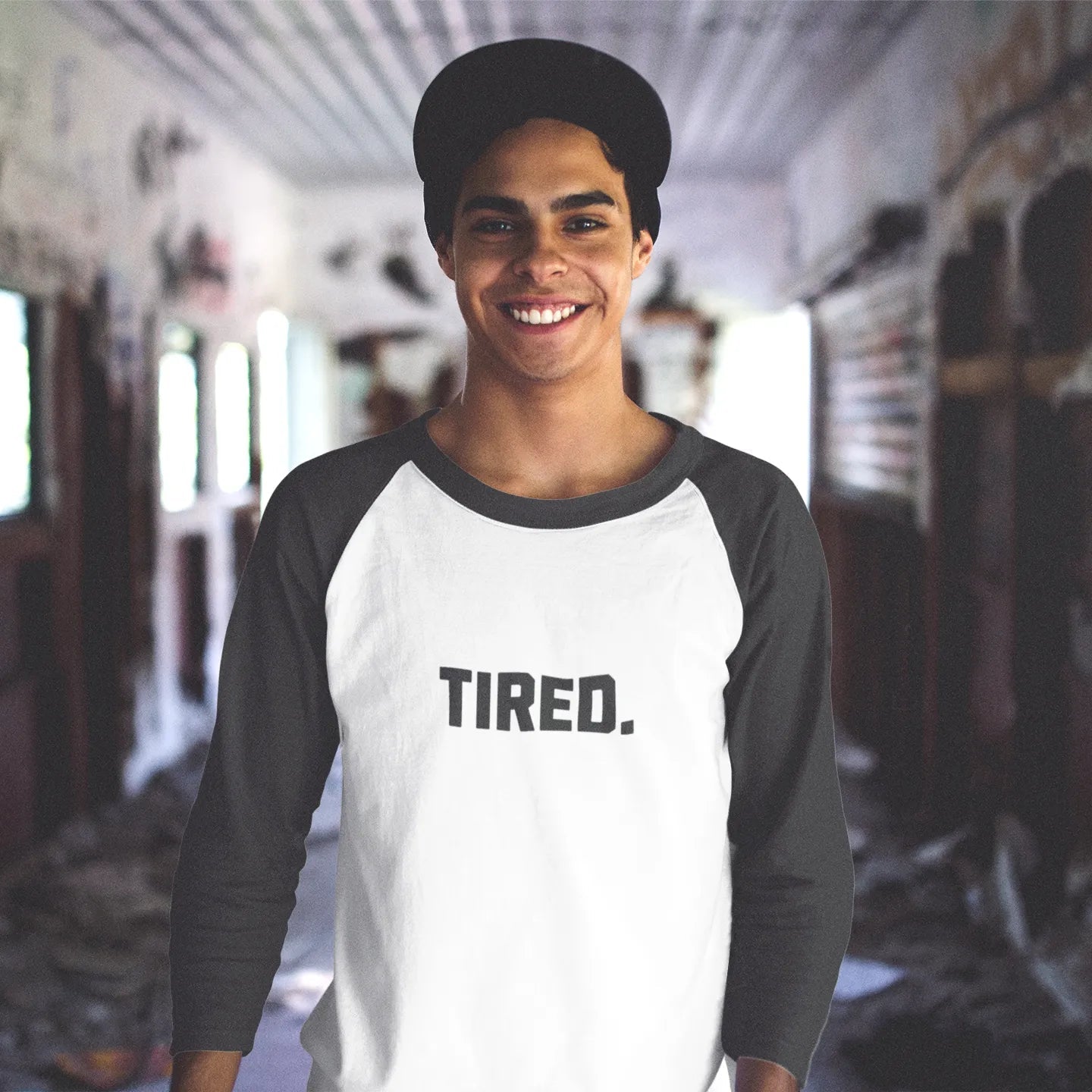 Person wearing a white and black baseball shirt with 'TIRED.' text in an indoor setting.