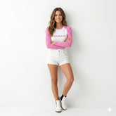 Woman wearing a pink and white long-sleeve shirt with 'Fearless' text, white shorts, and white boots on a white background.