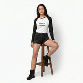Person wearing a black and white long-sleeve shirt with text, sitting on a stool against a white background