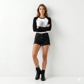 Woman wearing a black and white baseball shirt with text, black shorts, and black boots on a white background