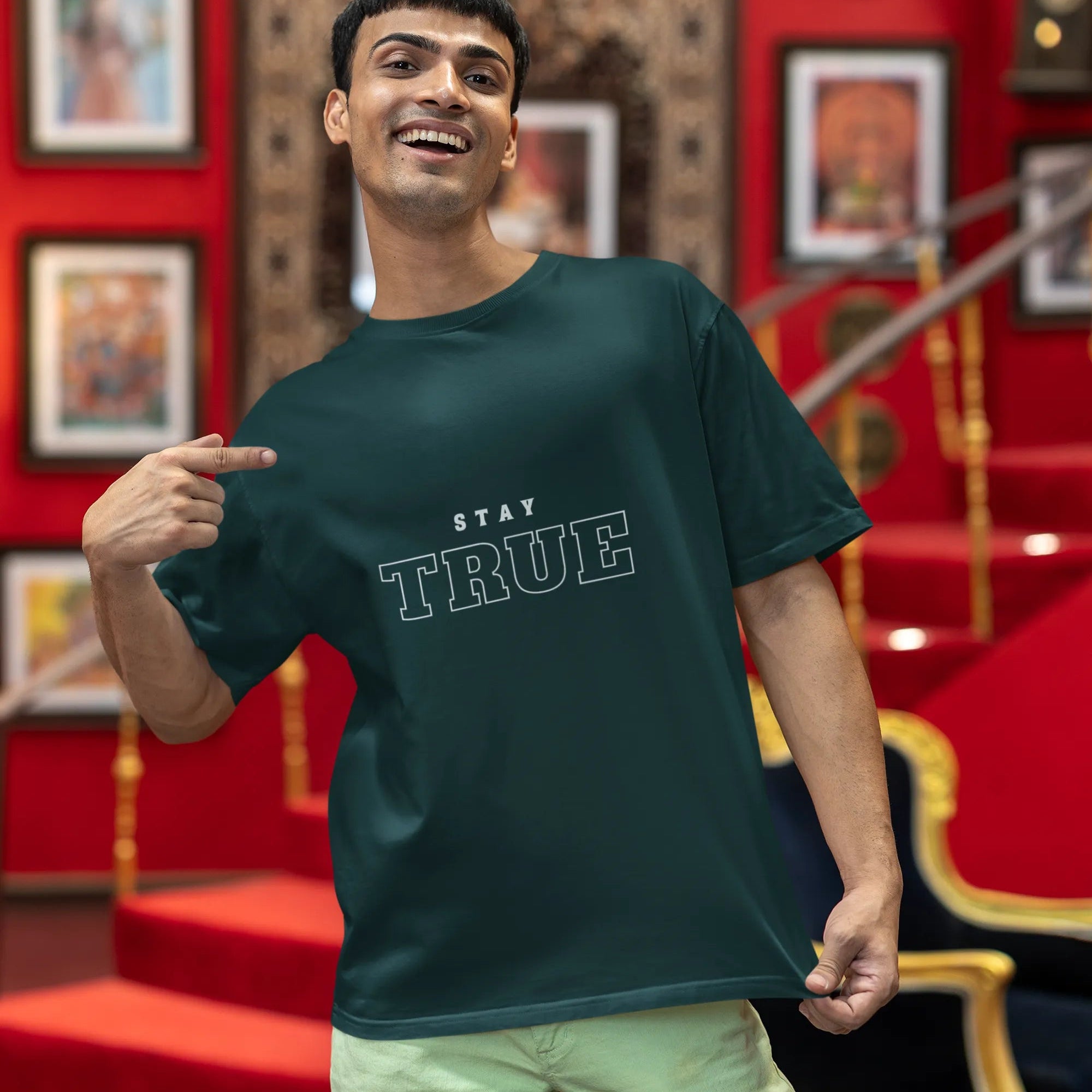 Man wearing a dark green t-shirt with 'Stay True' text in a decorative room.