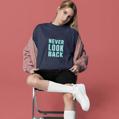 Woman sitting on a chair wearing a navy sweatshirt with 'NEVER LOOK BACK' text, white sneakers, and knee-high socks against a red background.