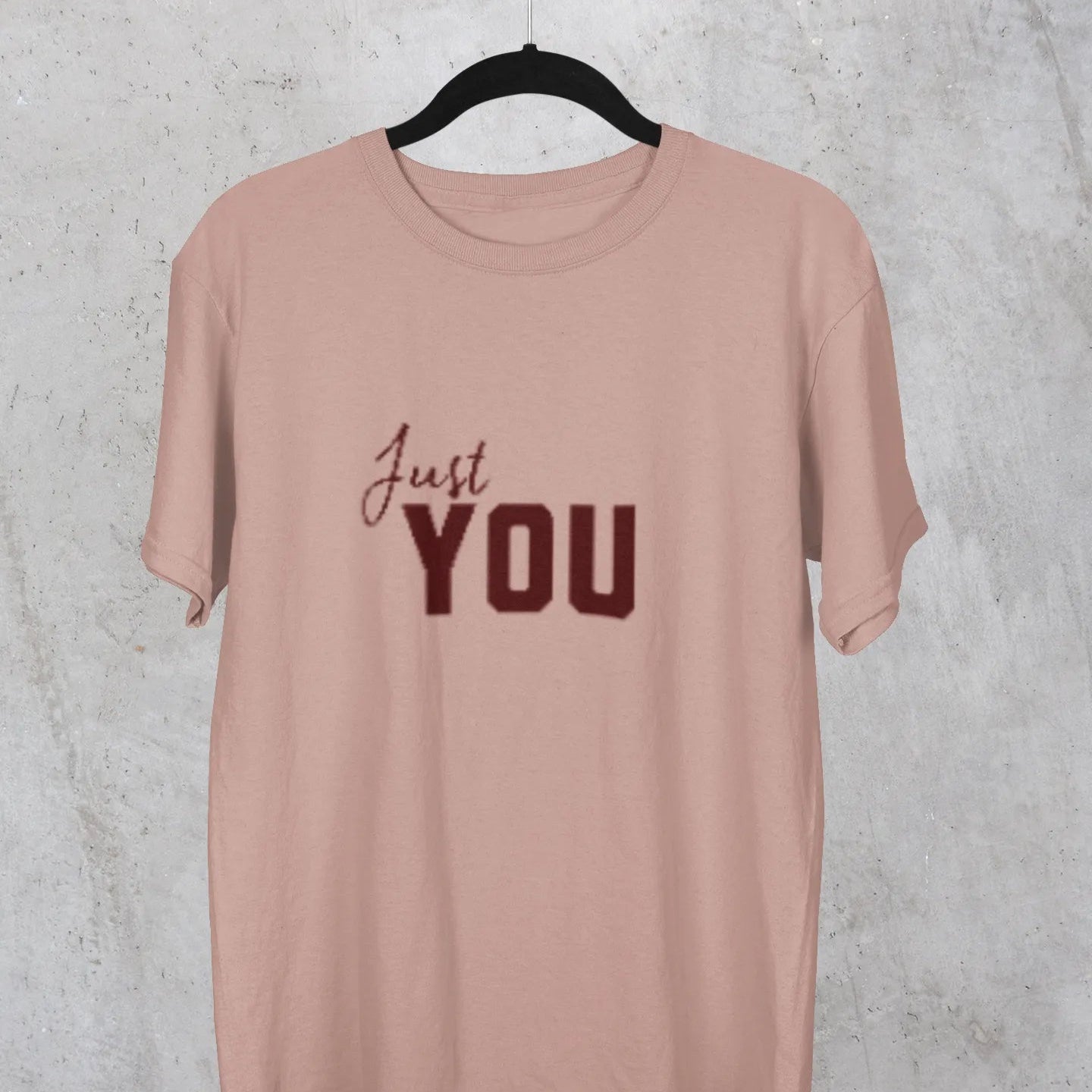 Pink t-shirt with 'Just YOU' text on a hanger against a textured gray background