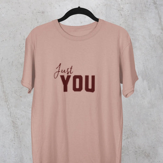 Pink t-shirt with 'Just YOU' text on a hanger against a textured gray background