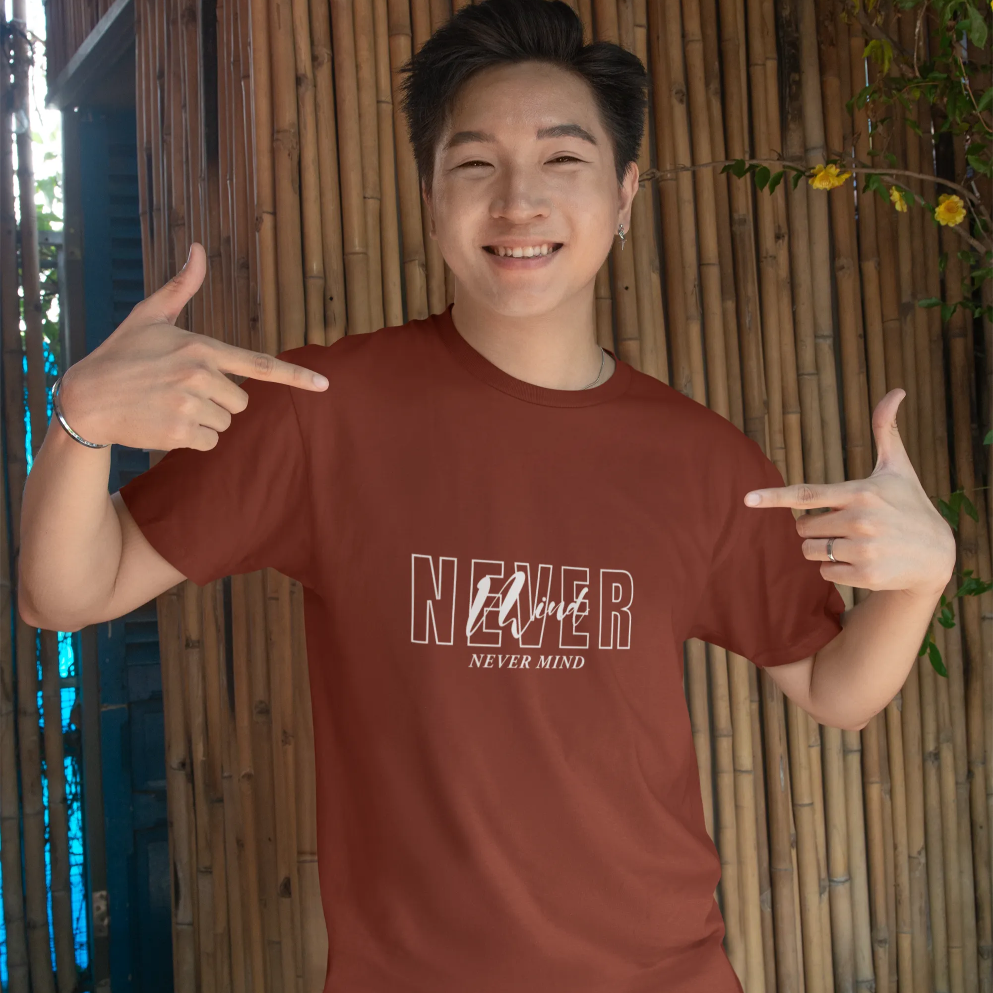 Person wearing a red t-shirt with text, pointing at the shirt against a bamboo wall background