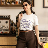Woman wearing a white t-shirt with text in a vintage room with shelves and decor.