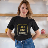 Woman wearing a black t-shirt with 'Bold Brave Strong' text in a yellow box, standing indoors.