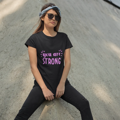 Person wearing a black t-shirt with 'you are STRONG' text, sitting on a concrete surface.