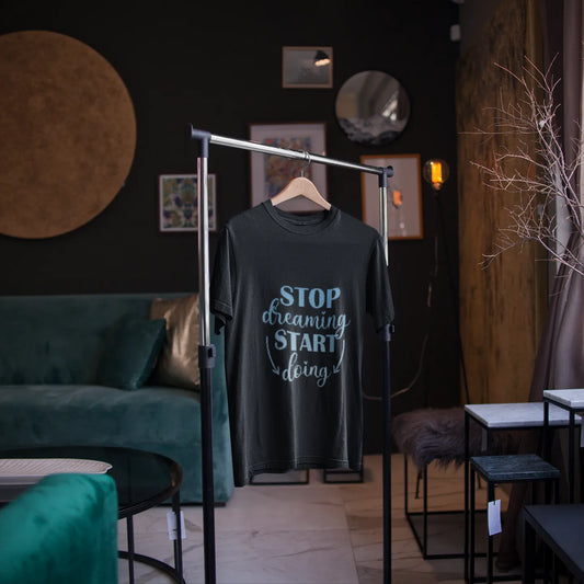 T-shirt with 'Stop dreaming, start living' text on a hanger in a room with a green sofa and decorative elements.