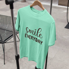 Mint green t-shirt with 'smile everyday' text on a hanger against a blurred indoor background