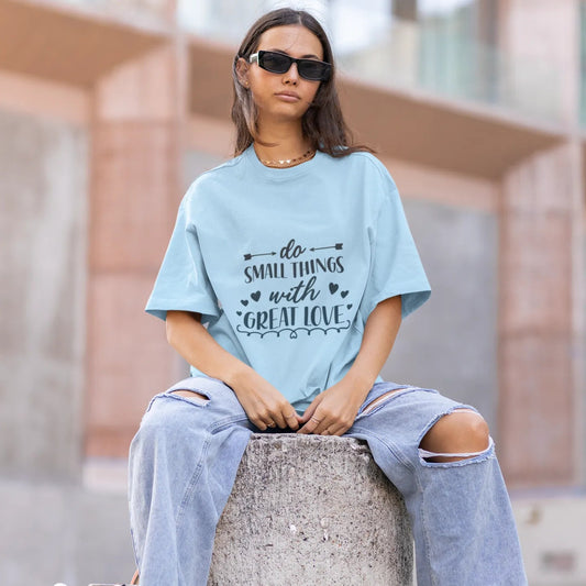 Person wearing a light blue t-shirt with text, sitting on a concrete block outdoors.