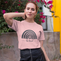 Woman wearing a pink t-shirt with a rainbow design and 'be kind' text, standing outdoors with flowers in the background.