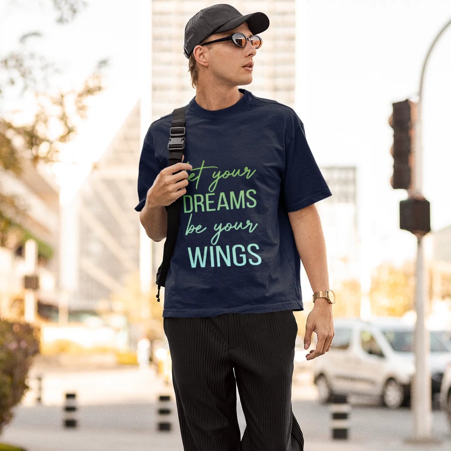 Man walking outdoors wearing a navy t-shirt with motivational quote, black pants, and cap.