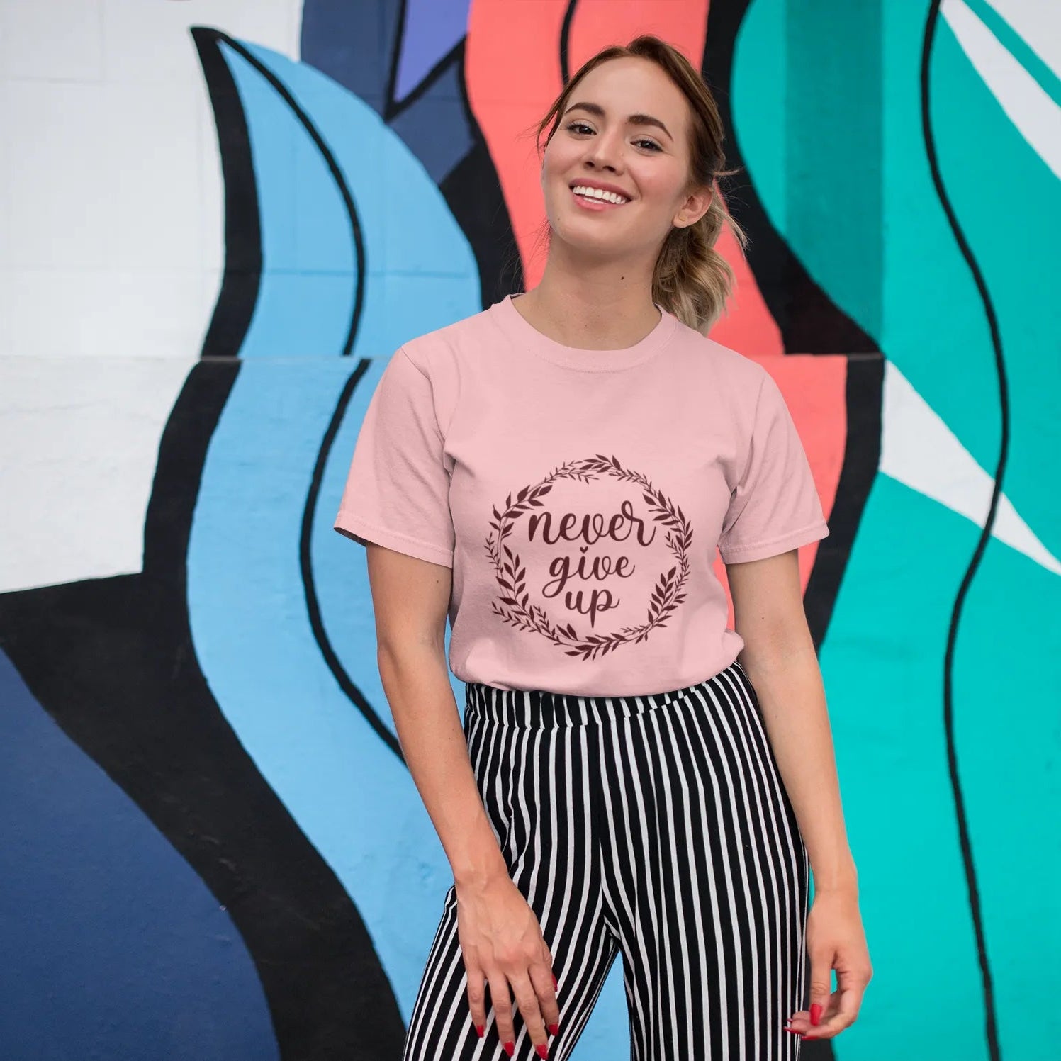 Woman wearing a pink t-shirt with 'never give up' text in front of a colorful mural.