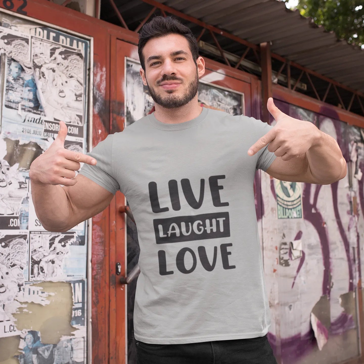 Man wearing a t-shirt with 'Live Laugh Love' text in front of a graffiti-covered wall.