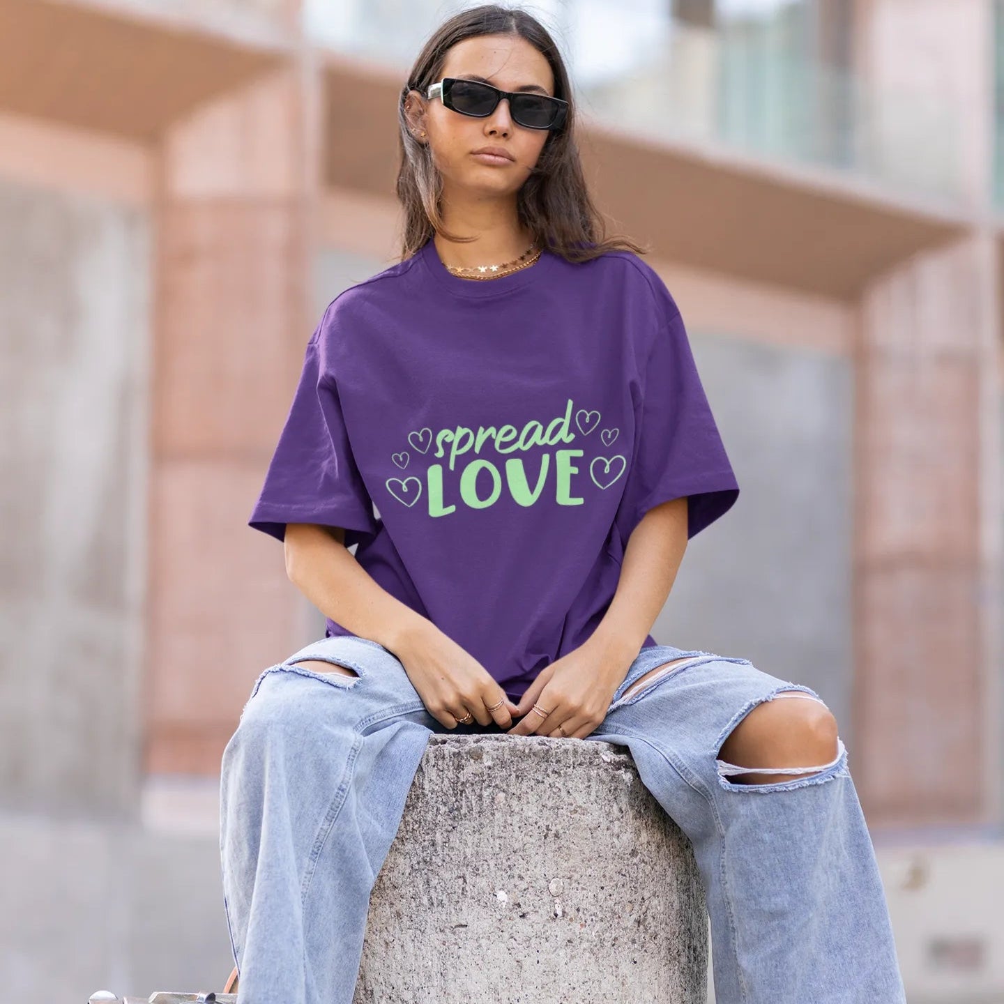 Person wearing a purple 'spread love' t-shirt sitting on a concrete block outdoors.