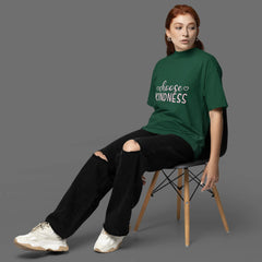 Person wearing a green t-shirt with 'Choose Kindness' text, sitting on a chair against a gray background