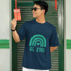 Person wearing a navy blue t-shirt with a green rainbow and 'BE KIND' text, standing in front of green shutters with red lanterns.