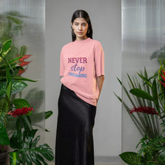 Woman wearing a pink t-shirt with text and a black skirt standing in a room with plants.