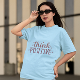 Woman wearing a light blue t-shirt with 'think positive' text outdoors.