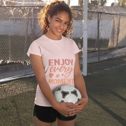 Girl holding a soccer ball on a sports field with 'Enjoy every moment' t-shirt