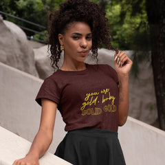 Woman wearing a brown t-shirt with yellow text, standing outdoors.
