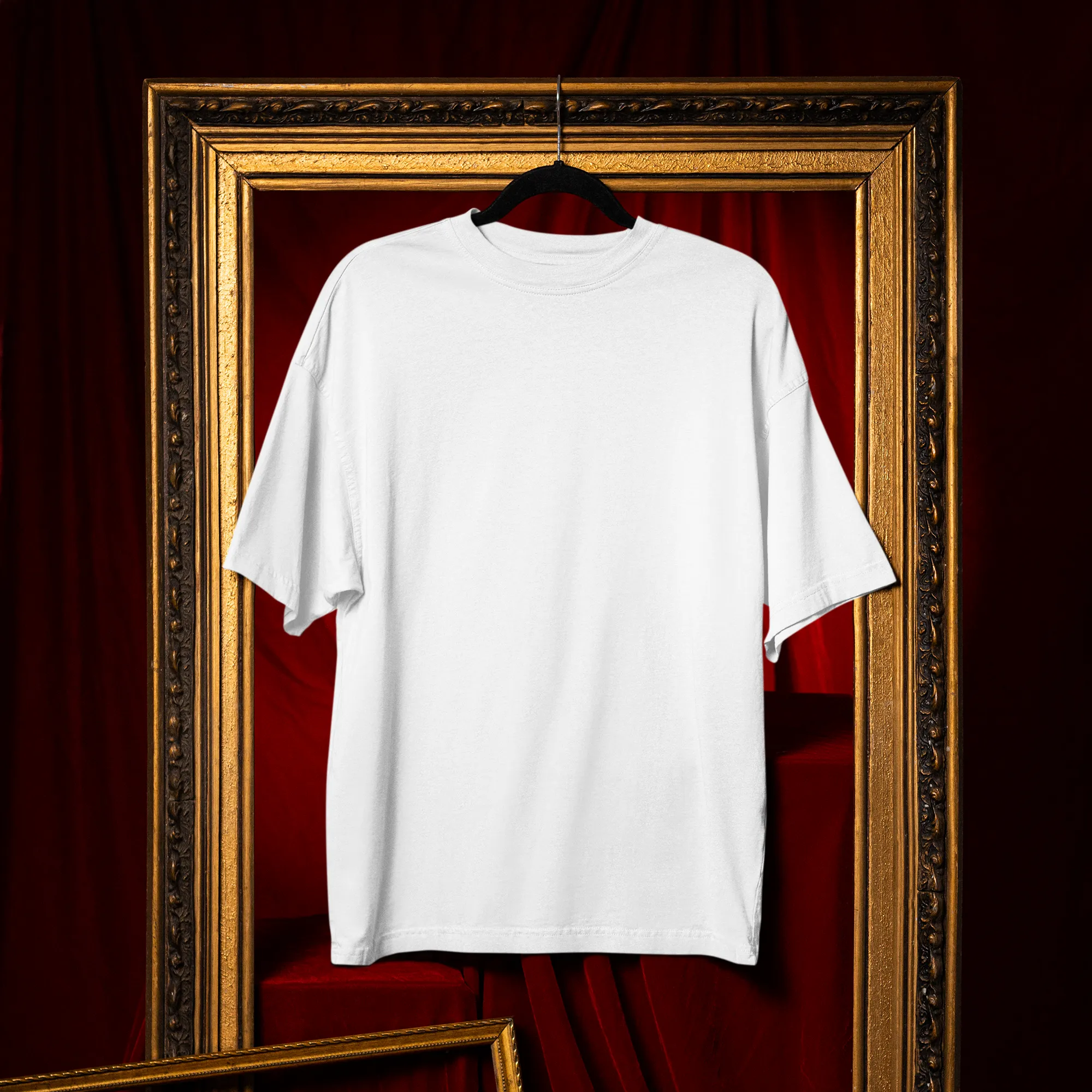 White t-shirt on a hanger inside an ornate gold frame with red curtain background