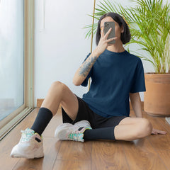 Person taking a mirror selfie in a room with a plant and lamp.