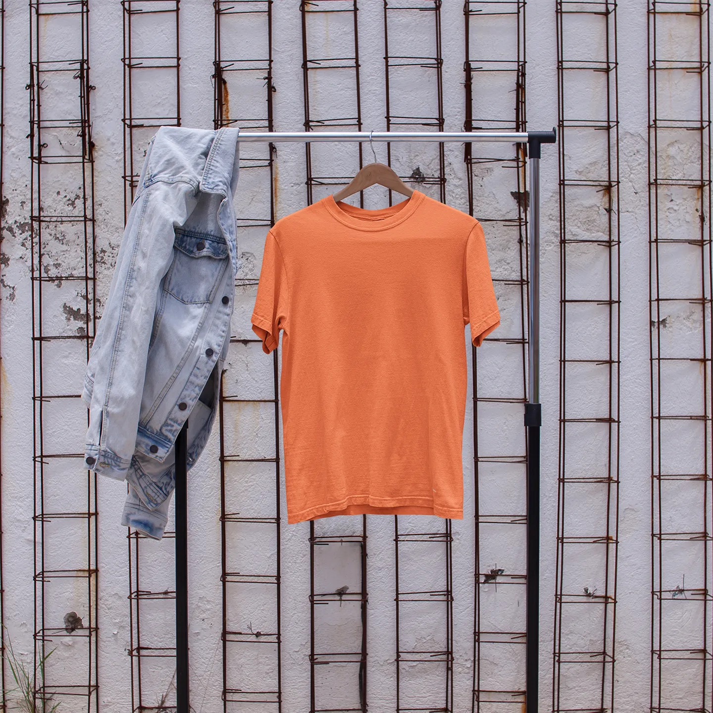 Orange t-shirt on a rack with denim jacket and white sneakers in front of a textured wall.