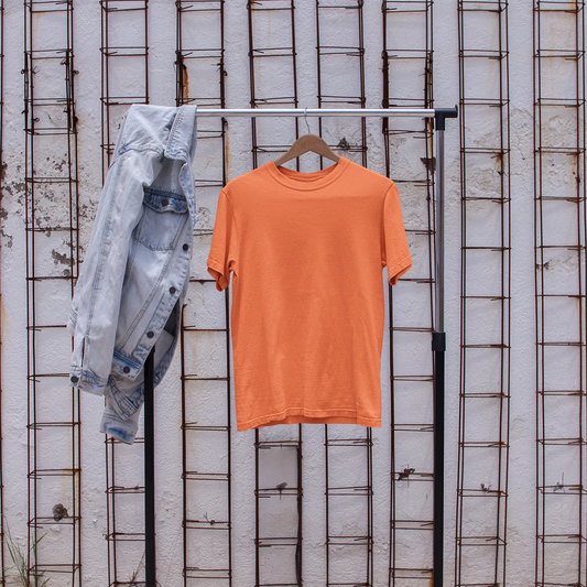 Orange t-shirt on a rack with denim jacket and white sneakers in front of a textured wall.