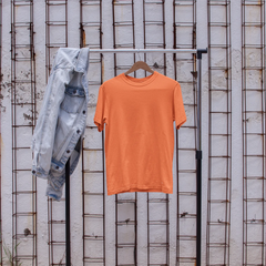 Orange t-shirt on a rack with denim jacket and white sneakers in front of a textured wall.