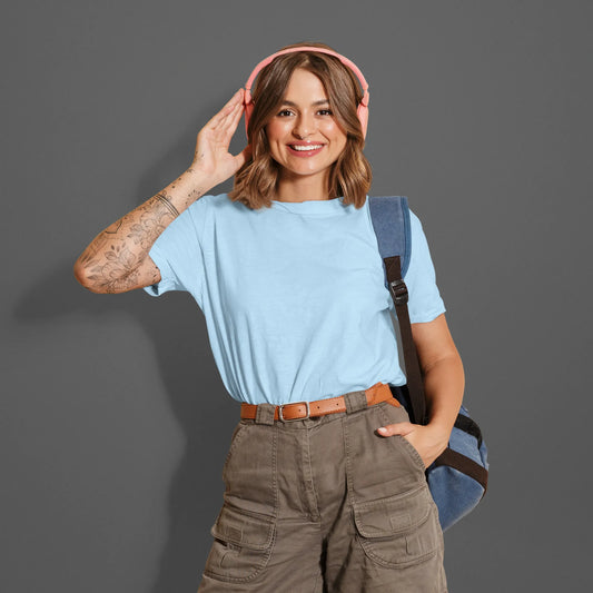 Woman wearing pink headphones, blue shirt, and brown pants against a gray background