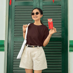 Woman holding red envelopes in front of a green shutter with red lanterns.