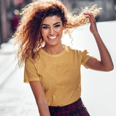 Woman with curly hair wearing a yellow shirt and plaid pants, smiling outdoors.