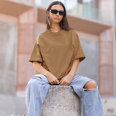 Person wearing a brown t-shirt and ripped jeans sitting on a concrete block.