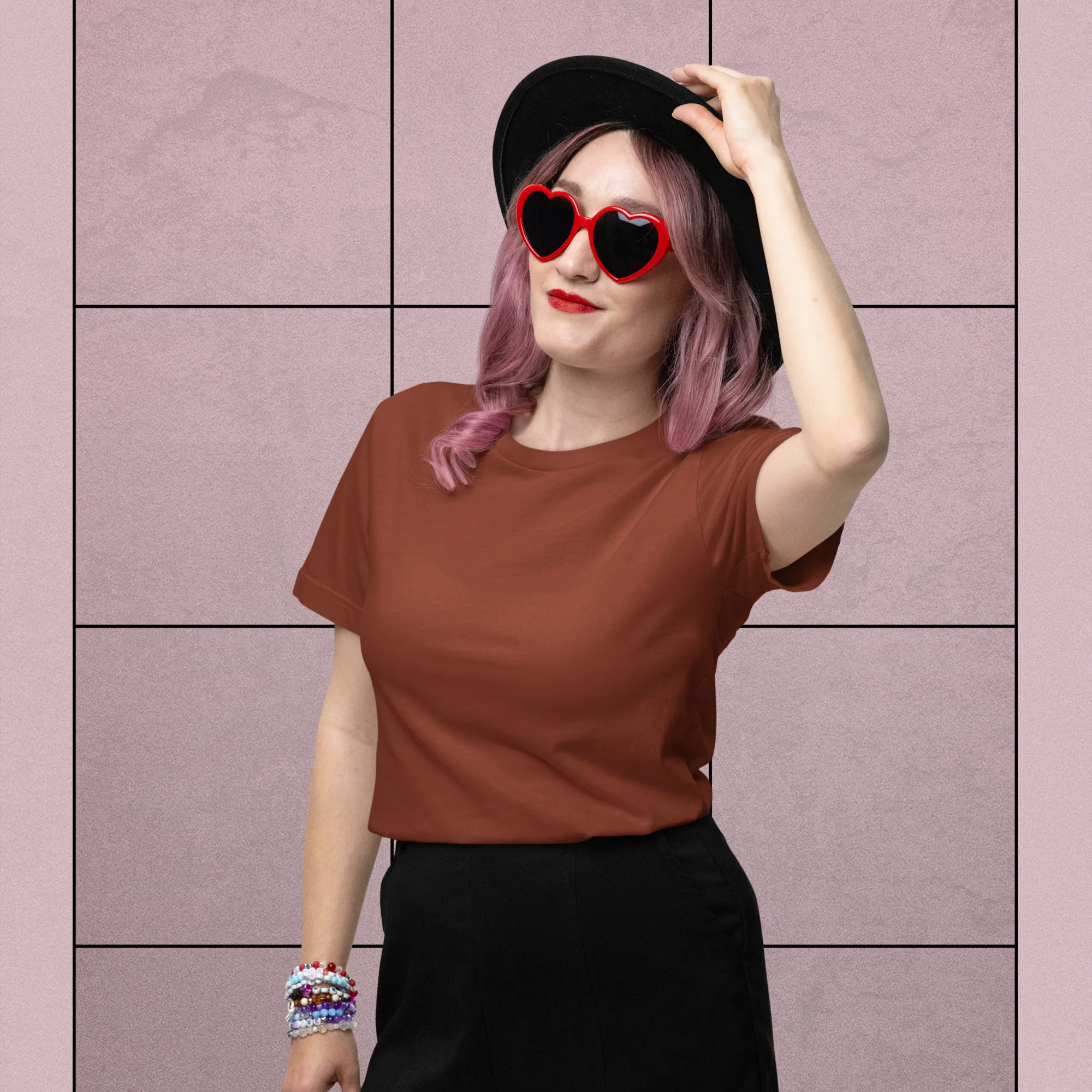 Person wearing a brown shirt and black shorts with heart-shaped sunglasses against a pink tiled wall.