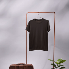 Black t-shirt on a copper stand with a brown suitcase, mirror, and potted plant on a gray background