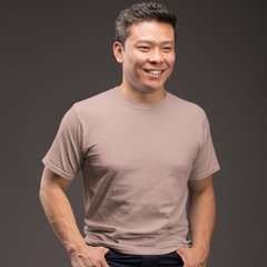 Man sitting on a stool wearing a beige t-shirt and dark pants against a gray background