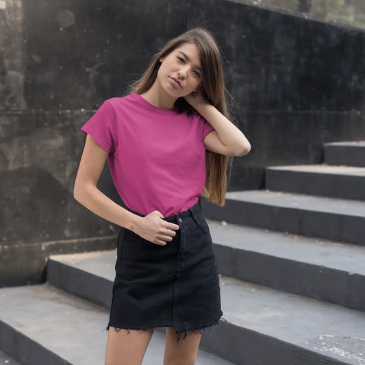 Woman in a pink shirt and black skirt standing on stone steps against a black wall.